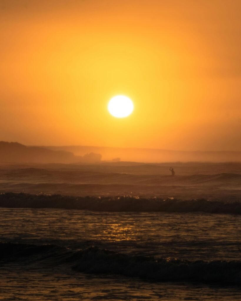 Serene view of a sunset at Warrnambool Beach with a silhouette on the waves.